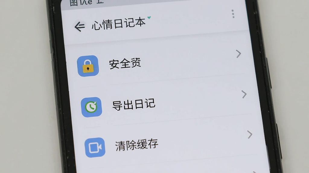 一部安卓手机屏幕显示「心情日记本」的设置页面,画面中有安全锁、导出日记、清除缓存等选项,背景为浅灰色,风格简洁实用,排版清晰,细节上设置项图标统一,画质清晰,干净,无多余元素