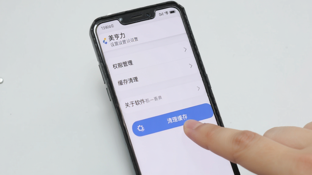 手机屏幕显示“美亨力”设置页面,页面中有权限管理、缓存清理、关于软件等选项,旁边有一只手正在点击“清理缓存”按钮,背景为浅灰色,整体风格简约实用,画质清晰,无多余元素。