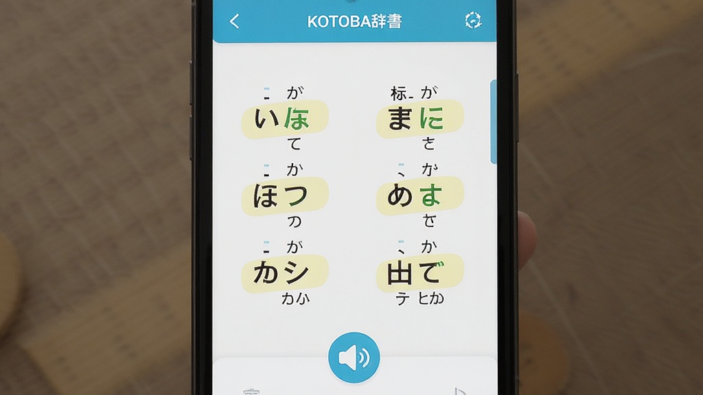 一张展示KOTOBA辞假名标注与发音功能的界面图,画面中央为手机屏幕显示日语单词与假名对照表,屏幕下方有喇叭图标,布局为居中展示,风格为清新学习类UI风格,细节包含高亮假名与音调标记,画质高清干净无多余元素
