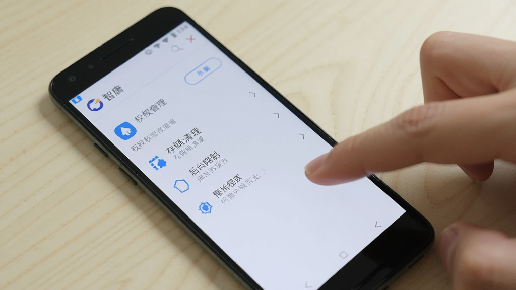 一部安卓手机屏幕显示“智唐”应用设置界面,界面上有权限管理、存储清理、后台限制等选项,旁边有一只手正在点击屏幕,背景为浅色桌面,风格简洁实用,画质清晰,无多余元素。