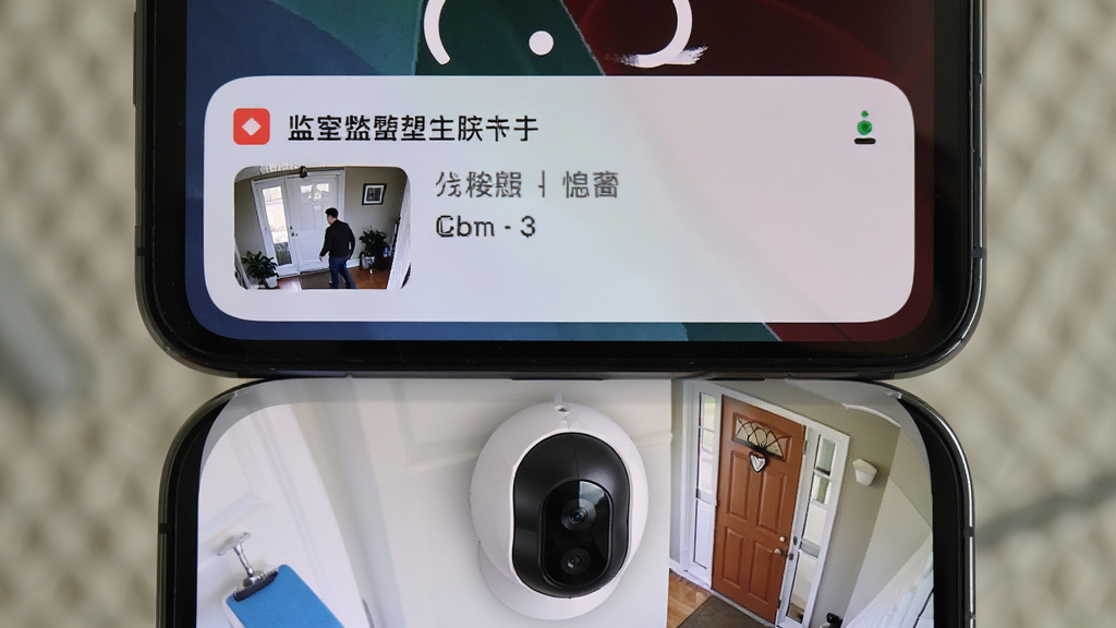 手机锁屏界面弹出一条监控报警通知,通知中显示一张门口有人经过的截图缩略图,手机下方有一个摄像头设备正对着门口,画面风格为写实摄影,光线自然,整体干净整洁,画质高清,无多余元素