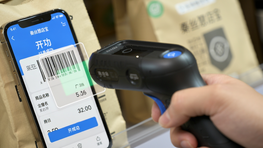手持蓝牙扫码枪对准商品条码进行扫描,画面主体为扫码枪与商品标签,布局为近景特写,排版突出扫码动作,风格为写实产品摄影,细节包含手机屏幕显示“秦丝慧店宝”开单成功界面、商品名称与价格,画质清晰,干净,无多余元素