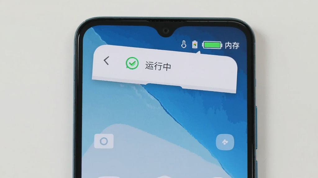 一部安卓手机显示自动点击全能王正在后台运行的提示,手机屏幕上方有悬浮窗显示“运行中”状态,旁边有电池图标和内存占用指示,背景为干净的桌面壁纸,风格简洁,画质清晰,无多余元素