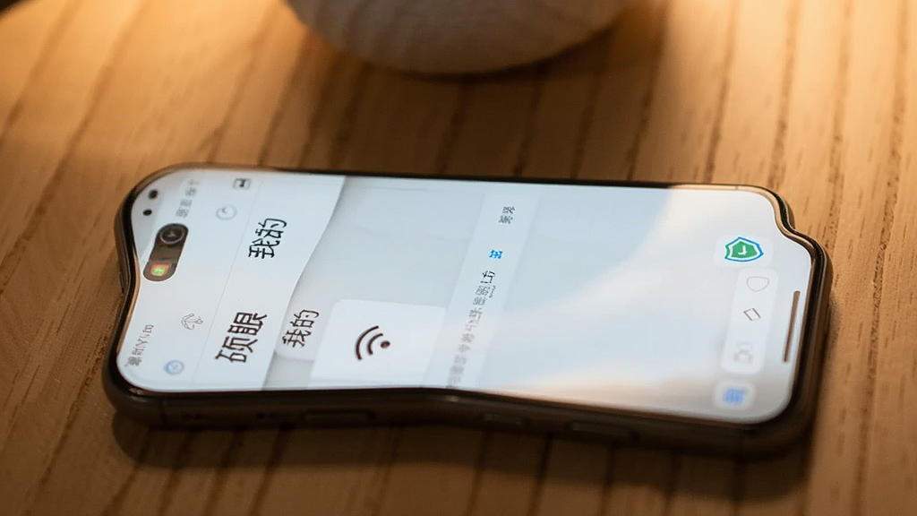 一部手机放置在木质桌面上,屏幕显示硕眼探企的“我的”页面,旁边有WiFi信号图标和盾牌安全图标,背景为柔和暖光,风格生活化,画质清晰,无杂乱物品