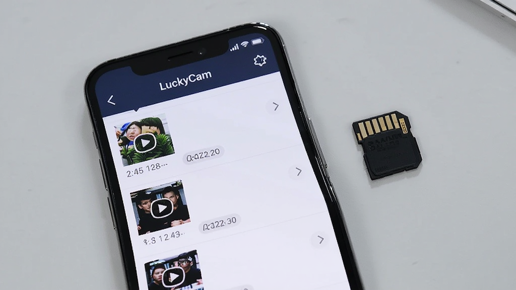 手机屏幕显示LuckyCam应用的文件列表界面,列表中有多个视频缩略图和日期标签,手机放在桌面上,旁边有一张内存卡,背景是浅灰色桌面,布局采用俯视平铺构图,风格为简洁产品展示风,细节包括屏幕界面文字清晰、内存卡金属触点可见,画质高清,干净,无多余元素。