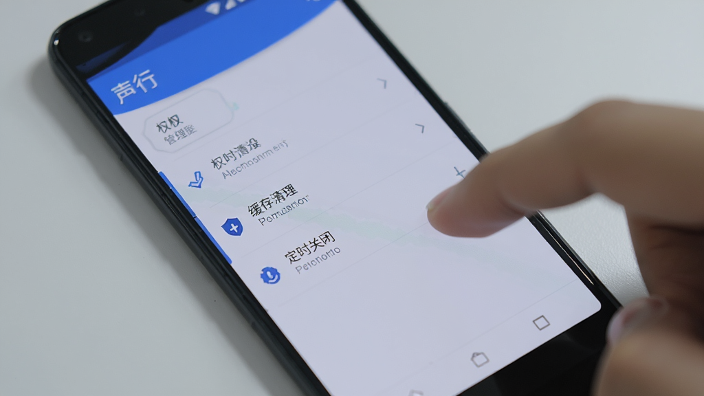 一部安卓手机屏幕特写,显示“声行”应用的设置页面,页面中有权限管理、缓存清理、定时关闭等选项,手机旁边有一只手正在点击屏幕,背景为浅灰色桌面,风格写实,排版清晰,细节可见,画质干净,无多余元素