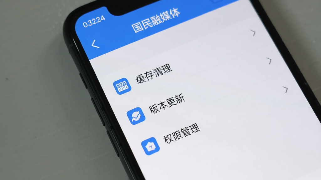 手机屏幕显示“国民融媒体”应用设置页面,页面中包含缓存清理、版本更新、权限管理等选项列表,界面采用浅色背景与蓝色图标点缀,风格简约实用,画质清晰干净,排版有序,无多余元素
