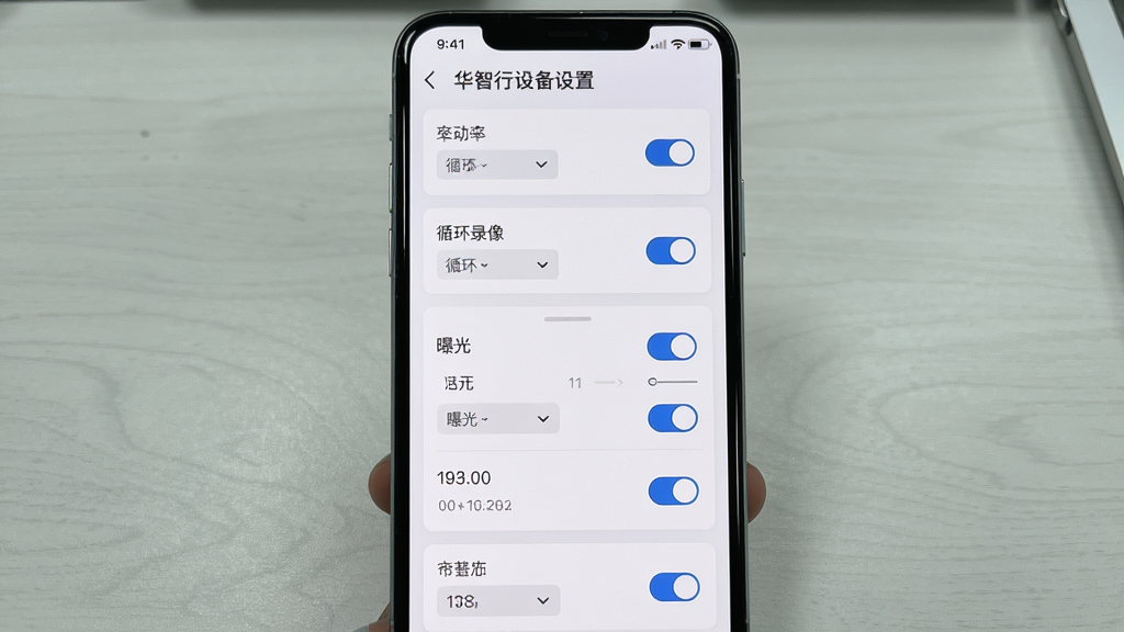 画面主体为华智行设备设置页面,屏幕中展示分辨率、循环录像、曝光等参数选项与开关按钮;布局为手机竖屏居中,背景为浅灰桌面;排版采用分组卡片式,每项设置独立成行;风格为简洁设置面板风;细节包含开关滑块、下拉菜单、参数数值;画质清晰,干净,无多余元素