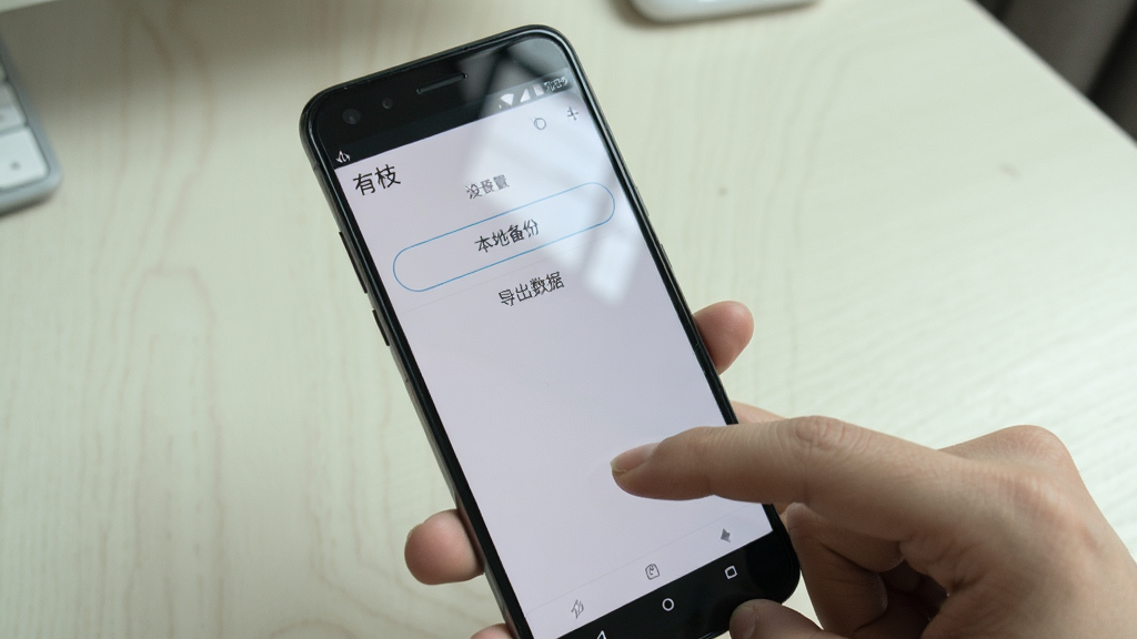 安卓手机操作场景图,画面展示一只手握持手机,手机屏幕显示“有枝”应用的设置页面,页面中有“本地备份”“导出数据”等选项按钮,背景为简洁的浅色桌面环境,风格真实生活化,细节包含手指点击动作与屏幕反光,画质清晰干净,构图聚焦手机屏幕,无多余杂物