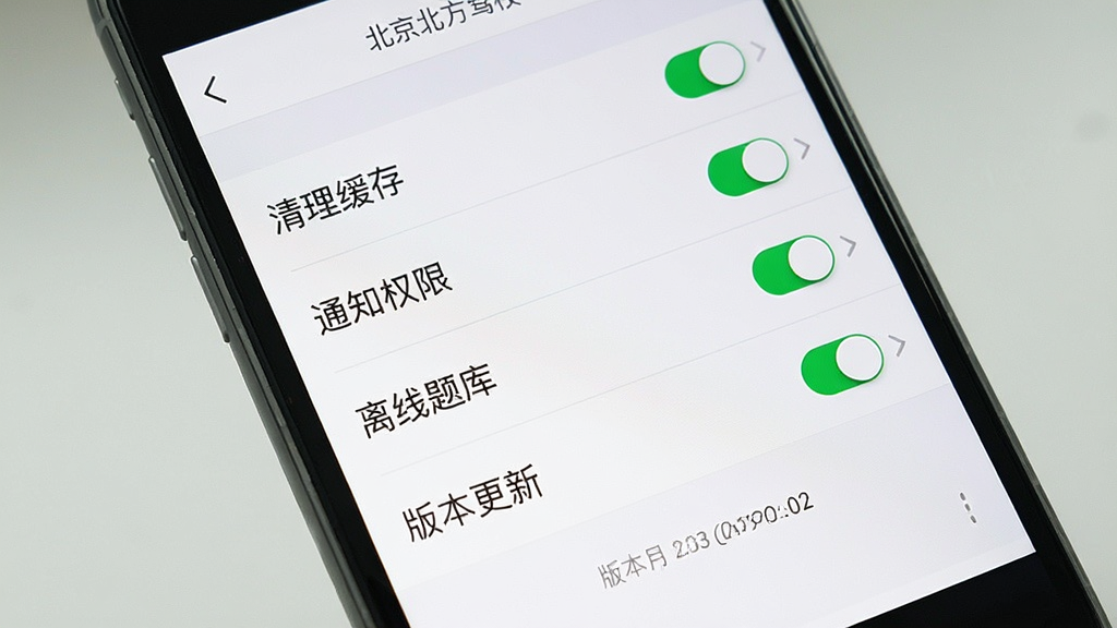 画面主体为手机屏幕展示驾培应用设置页面,列表中包含“清理缓存”“通知权限”“离线题库”“版本更新”四个条目,右侧配开关或箭头图标;布局为纵向列表,顶部有“北京北方驾校”小字;风格为简洁设置页UI风,配色以白色与浅灰为主;细节包括条目分割线、开关状态高亮、底部版本号文字;画质清晰,画面干净,无多余元素。