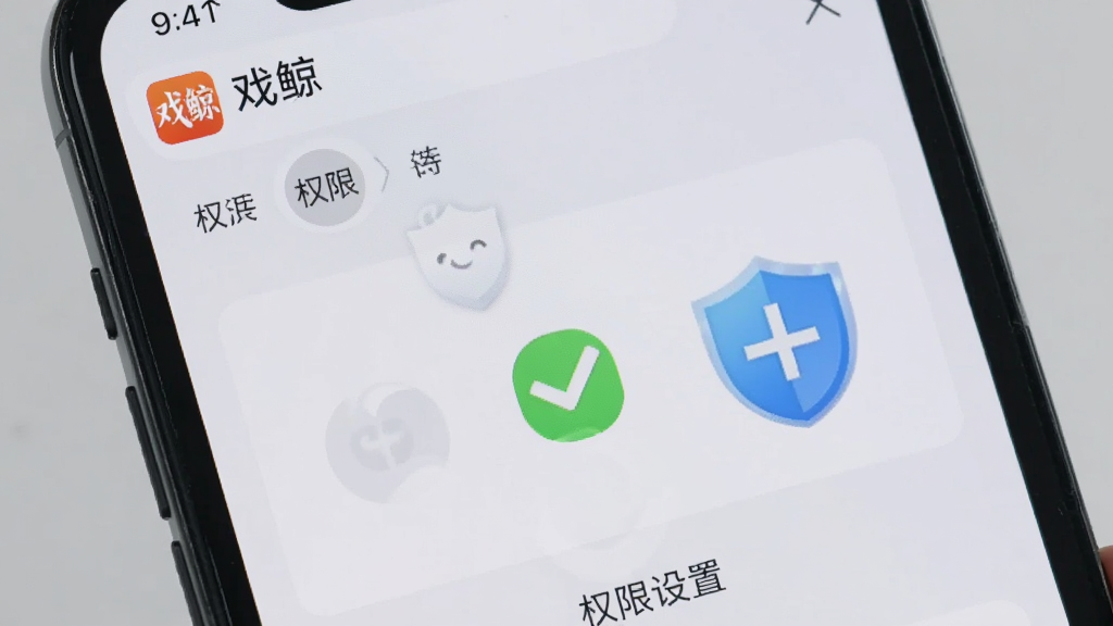 画面展示一部手机屏幕显示“戏鲸”App的权限设置页面,旁边有勾选标记和盾牌图标,背景为浅灰色,风格简洁明了,画质干净清晰,突出安全设置主题