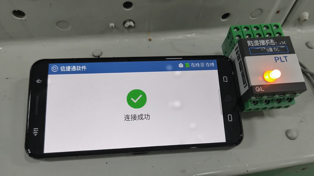 画面主体为一部横放的安卓手机,屏幕显示信捷通软件的设备连接状态页面,页面中央有绿色对勾图标与“连接成功”文字,顶部状态栏显示在线标识;手机旁边放置一个小型指示灯亮起的PLC模块;风格为工业现场实拍感,光线自然,构图简洁,细节真实,画质干净