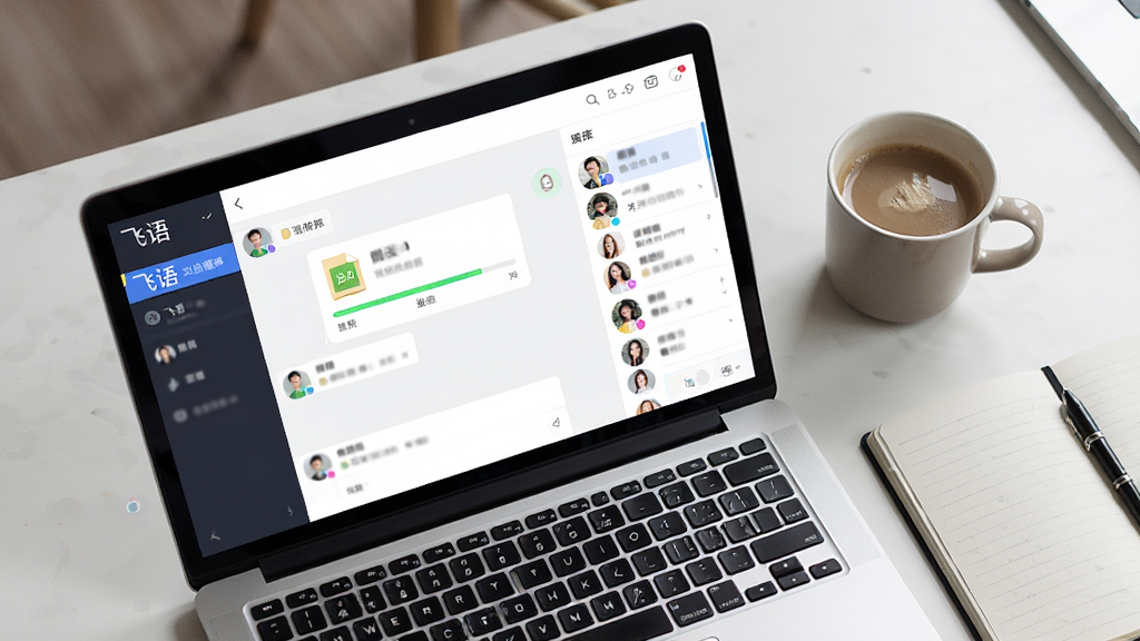 一张俯视视角的桌面,桌面上有一台打开的笔记本电脑,屏幕显示“飞语”群聊界面,聊天窗口中有文件传输进度条与群成员头像列表,旁边放着一杯咖啡和一本笔记本,风格为写实办公场景,光线柔和,画质清晰,画面整洁