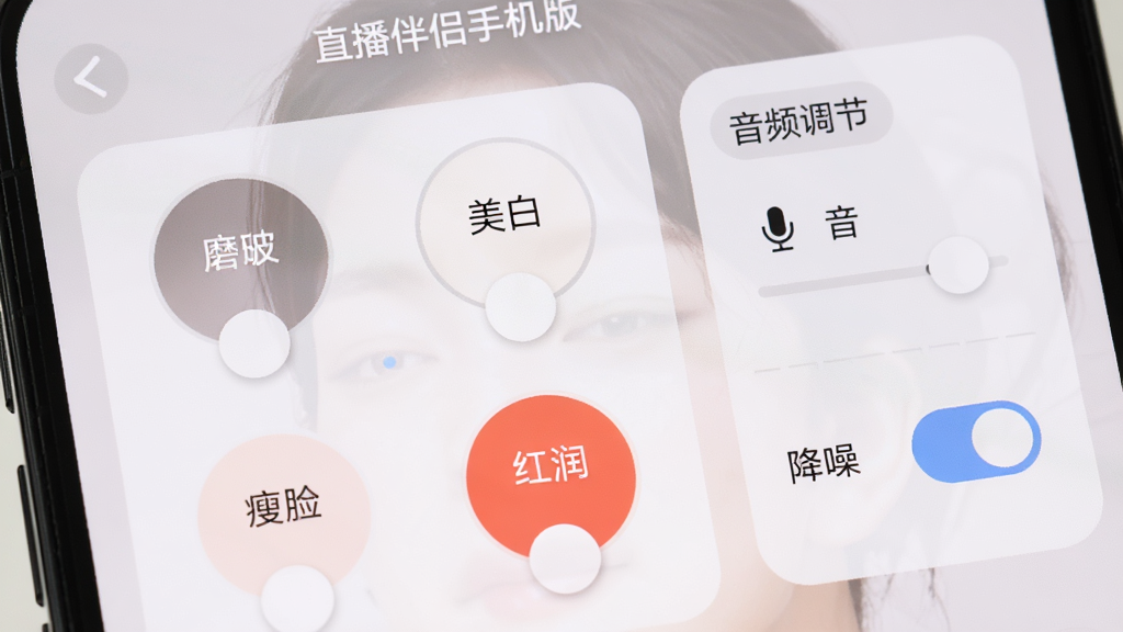 手机屏幕近景,展示“直播伴侣手机版”的美颜调节界面,画面中有四个圆形滑块分别控制磨皮、美白、瘦脸和红润,右侧为音频调节面板包含麦克风音量和降噪开关,界面采用浅色圆角卡片设计,风格清新柔和,细节丰富,画质清晰,无杂乱元素