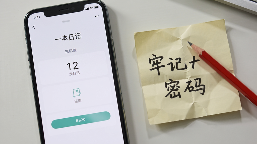 画面主体为一部手机屏幕显示“一本日记”的密码设置界面,旁边放置一张手写便签写着“牢记密码”四个中文字,便签上压着一支红色铅笔,背景为浅灰色桌面,整体布局左机右签,风格生活化提示感,细节上突出便签纸的折痕与铅笔阴影,画质清晰干净,无多余元素