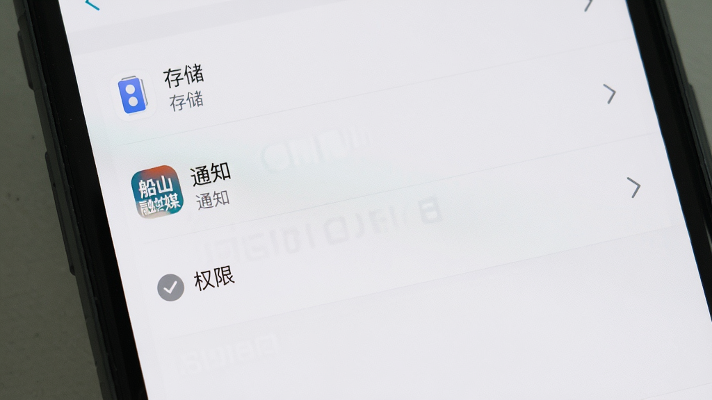 手机应用设置界面展示权限管理与缓存清理选项,主体为手机屏幕特写,布局上屏幕居中显示设置列表,排版为纵向条目排列,风格为简洁系统设置界面风格,细节上包含“存储”“通知”“权限”等选项与“船山融媒”应用图标,画质清晰、画面干净、无多余元素