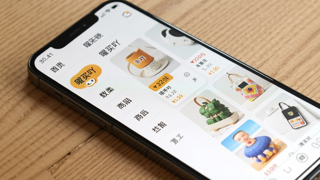 画面主体是一部手机斜放在木质桌面上,屏幕显示“曜买吖”的商品分类页面,左侧为分类导航栏,右侧为商品网格列表;布局采用对角线构图,手机占据画面主要位置;排版上分类标签与商品卡片排列整齐;风格为清新简约的电商界面展示风;细节上商品图片色彩鲜明,价格标签用暖色突出;画质干净清晰,背景无杂乱物品,光线柔和自然。