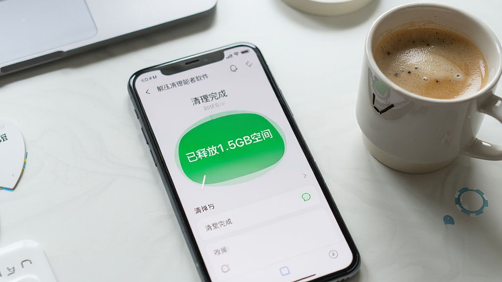 解压清理能者软件在手机上运行的实拍图,手机屏幕显示清理完成后的界面,显示“已释放1.5GB空间”的绿色大字,背景为整洁的桌面,手机旁边放着一杯咖啡,整体风格生活化,画质清晰,无多余元素。