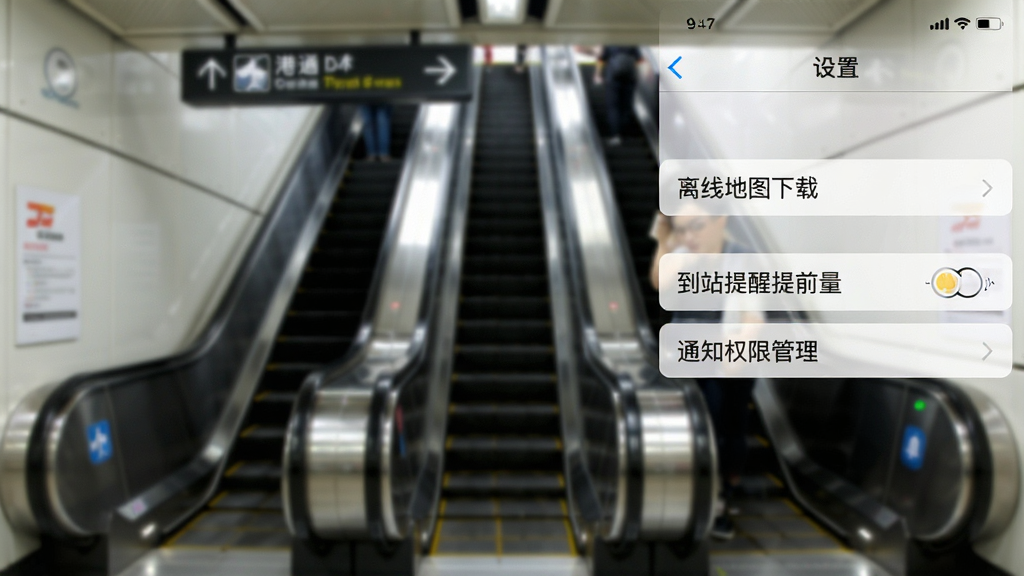 一张手机截图风格的图片,屏幕显示“港铁通”应用的“设置”页面,包含“离线地图下载”、“到站提醒提前量”、“通知权限管理”等选项,背景为模糊的港铁站内自动扶梯,整体风格简洁,UI设计清晰,画质干净无多余元素