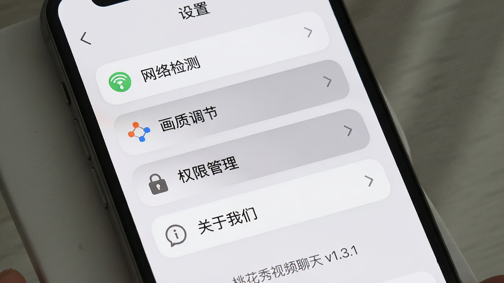 主体:手机屏幕展示桃花秀视频聊天“设置”页面,包含网络优化、画质调节、权限管理选项。布局:列表式菜单,每行有图标和文字。排版:从上到下依次为“网络检测”、“画质调节”、“权限管理”、“关于我们”。风格:简洁清晰。细节:页面背景为浅灰色,菜单项有圆角边框,选中项高亮,底部有“桃花秀视频聊天 v1.3.1”字样。画质:高清,干净,无多余元素。
