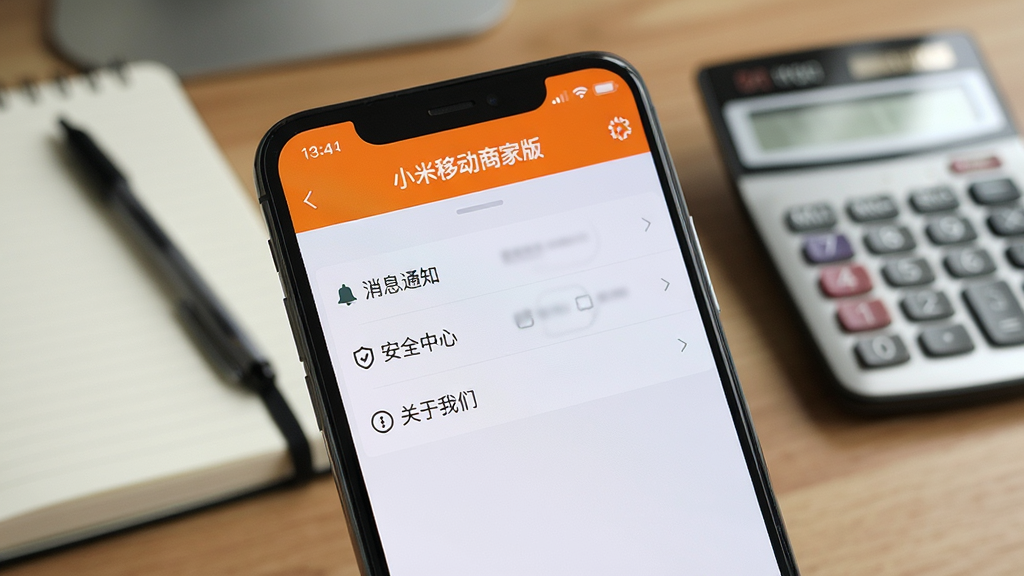 画面主体为一部手机正在显示“小米移动商家版”的设置界面,界面中有“消息通知”、“安全中心”、“关于我们”等选项。布局为手机屏幕特写,背景为模糊的办公桌面,放有笔记本和计算器。排版简洁明了,风格为写实摄影风格,细节上突出屏幕内文字的清晰度,画质锐利,整体氛围专业且安静。