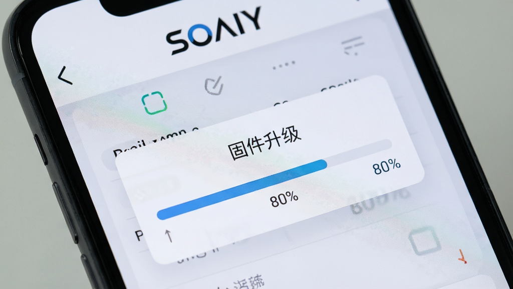 一张手机屏幕显示SOAIY软件操作界面的特写,页面中有一个“固件升级”弹窗,进度条显示80%,背景为浅灰色,上方有“SOAIY”品牌标识,画面写实,聚焦清晰,画质干净,无多余元素。