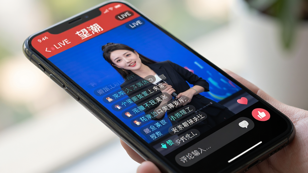 主体:一个正在播放直播的手机屏幕特写,屏幕中显示望潮APP直播界面,有主持人画面和弹幕飘过。布局:手机斜放,背景虚化。排版:直播界面下方有评论输入框和点赞按钮。风格:写实风格,光线明亮。细节:弹幕文字清晰可见,画面生动。画质:高清,干净,无多余元素。