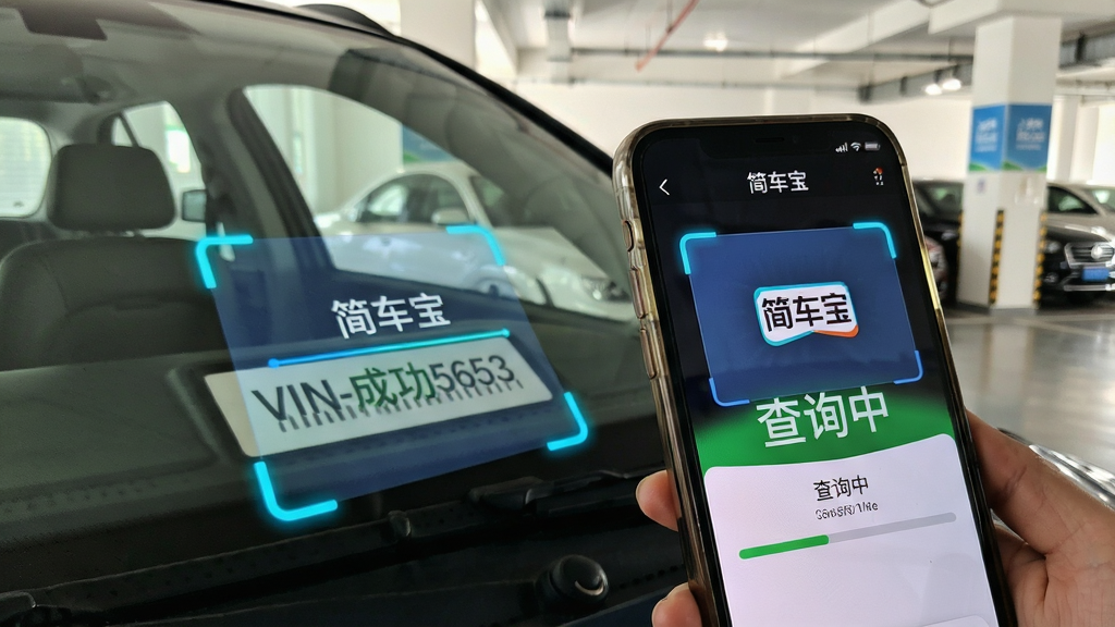 一张特写图片,展示一部智能手机正在扫描车辆前挡风玻璃下的VIN码区域,屏幕中清晰显示“简车宝”识别动画和扫描框,界面高亮识别成功的号码,并弹出“查询中”的进度条,背景是光线充足的室内停车场,风格写实,画质清晰
