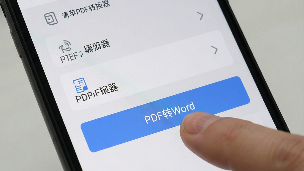 青苹PDF转换器在手机上的使用界面,智能手机屏幕显示软件功能列表,手指点击“PDF转Word”按钮,背景为浅灰色,界面简洁,高清画质,突出移动端操作便捷性