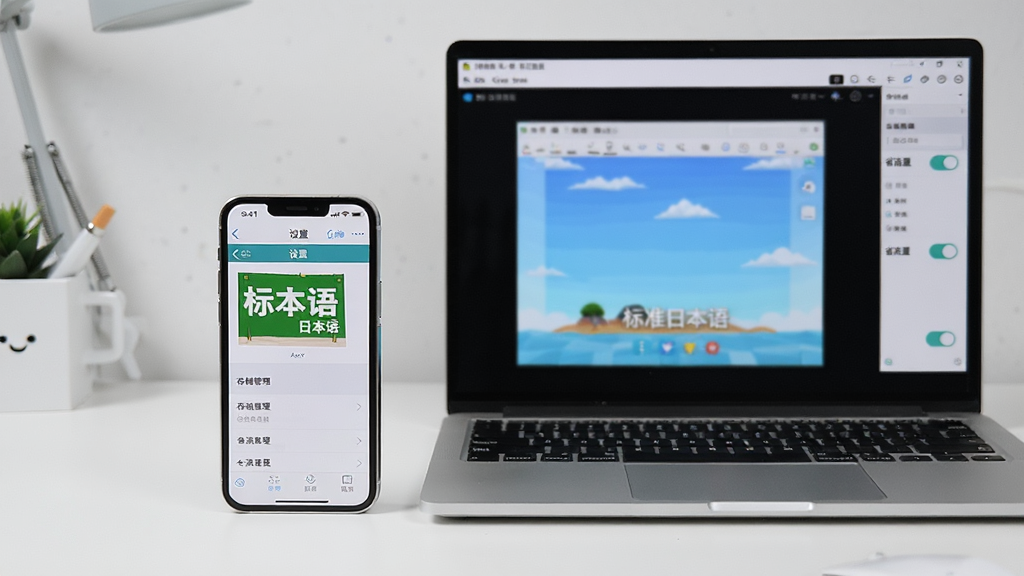 主体为手机与电脑并排摆放,手机屏幕显示《标准日本语》App的“设置”页面,电脑屏幕显示模拟器界面,背景为简洁工作台,布局左右均衡,风格现代简洁,细节包括“存储管理”与“省流量”开关,画质清晰干净,无多余元素