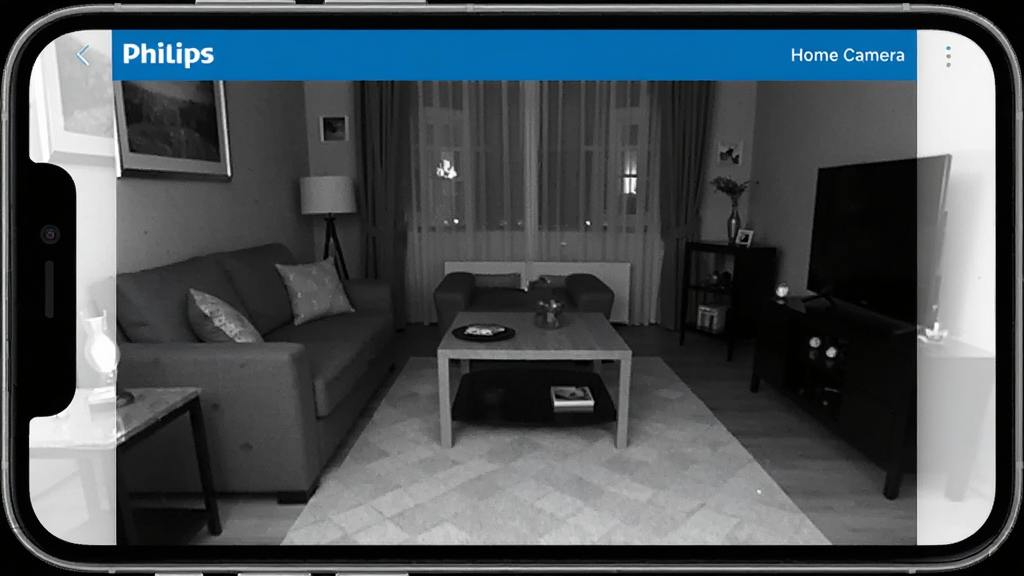 飞利浦摄像头在暗光环境下拍摄的客厅画面,手机应用Philips Home Camera界面显示黑白夜视效果,画面中沙发、茶几轮廓清晰可见,风格写实,布局对称,细节丰富,画质干净,无多余元素,应用界面文字标注