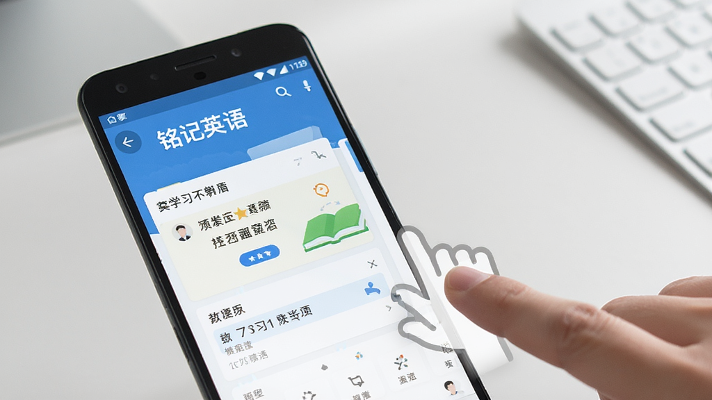 一张展示“铭记英语”在安卓手机上运行的操作示意图,画面中手机屏幕显示学习界面,旁边有手指点击的示意动作,背景为简洁的桌面环境,风格真实清晰,细节丰富,画质干净,无多余元素