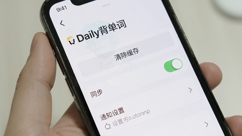 主体是手机屏幕显示Daily背单词的设置页面,布局为列表式,排版中带有“Daily背单词”标题,风格为简约实用风,细节包含清除缓存按钮、同步开关和通知设置,画质清晰,干净,无多余元素