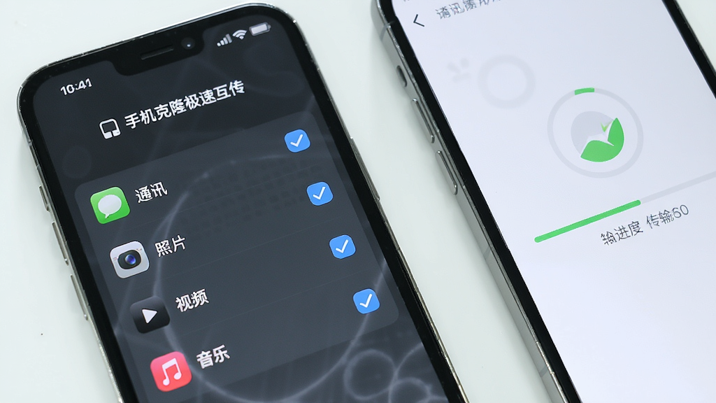 一部手机显示“手机克隆极速互传”的数据选择界面,屏幕上有通讯录、照片、视频、音乐等勾选项,旁边另一部手机显示传输进度,背景为简洁的白色桌面,画面风格清新明亮,画质清晰,干净无多余元素