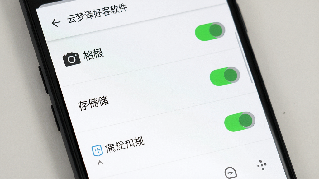 主体为一部安卓手机屏幕特写,屏幕上显示云梦泽好客软件的权限设置界面,包含相机、存储和通知权限开关。布局采用垂直列表排列,开关按钮清晰可见。排版简洁直观,风格为移动端系统设置界面风格,细节上开关有绿色和灰色两种状态,背景为纯白色,画质高清干净,无多余元素。