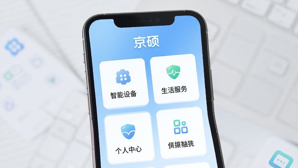 手机屏幕中央展示“京硕”应用主界面,顶部有“京硕”文字标识,界面布局为卡片式功能入口,包含智能设备、生活服务、个人中心等模块,背景为浅蓝色渐变,风格简洁现代,细节清晰,画质干净,无多余元素