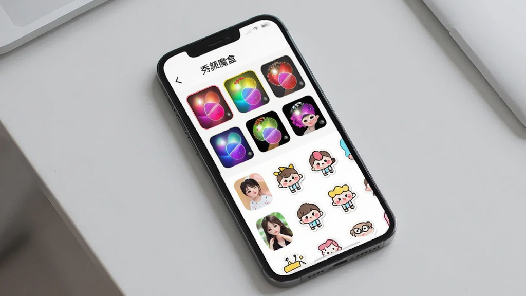 一张展示手机屏幕上排列着多种滤镜和贴纸素材的图片,画面中手机屏幕显示“秀颜魔盒”的素材选择界面,包含色彩丰富的滤镜缩略图和卡通贴纸图标,背景是浅灰色桌面,整体风格简约现代,画质干净,无多余元素