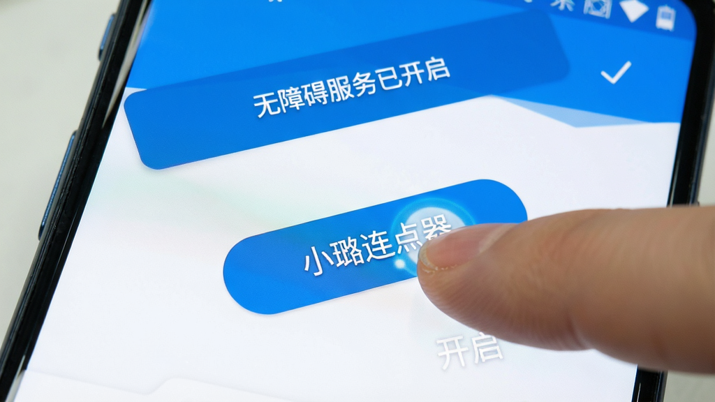 一部安卓手机屏幕特写,画面中手指正在点击“小璐连点器”的开启按钮,屏幕上方显示“无障碍服务已开启”的提示条,界面以蓝白配色为主,风格简洁明快,细节表现按钮的光影反馈,画质清晰,干净无多余元素。