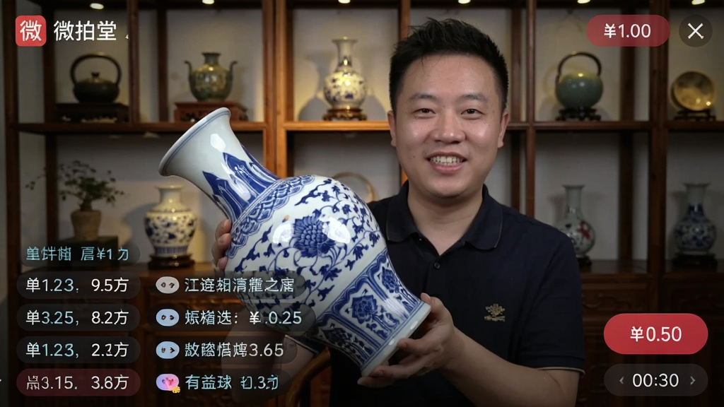 画面主体为一位商家在直播间内手持一只青花瓷瓶,面带微笑向镜头展示,屏幕下方有不断滚动的出价记录与用户弹幕。背景是布置雅致的文玩陈列架,灯光聚焦在瓷器上。布局采用竖屏直播界面风格,左上角有“微拍堂”标识,右侧有出价按钮与倒计时。风格为真实直播截图感,细节包括瓷器釉面反光、弹幕文字清晰、出价数字跳动,画质清晰,干净,无多余元素